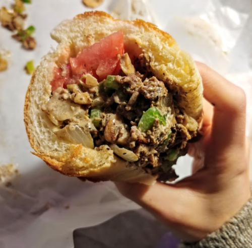A hand holding a sandwich filled with chopped vegetables and a creamy mixture, with a slice of tomato visible.