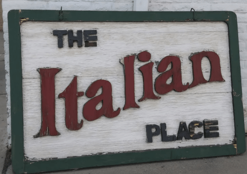 Sign for "The Italian Place" with bold red and black lettering on a weathered white background.