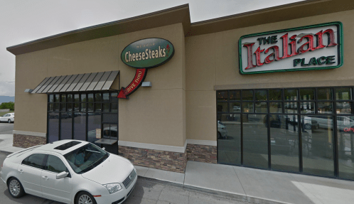 Exterior view of a building featuring two restaurants: "CheeseSteaks" and "The Italian Place," with a parked white car.