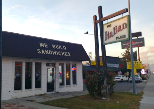 A sandwich shop called "The Italian Place" with a sign and bright windows, located on a busy street.