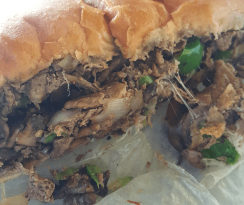 Close-up of a sandwich filled with shredded meat, onions, and green peppers, with melted cheese stretching from the filling.
