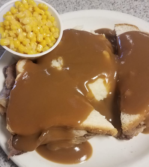 A plate with two slices of bread topped with roast beef and gravy, accompanied by a side of corn.