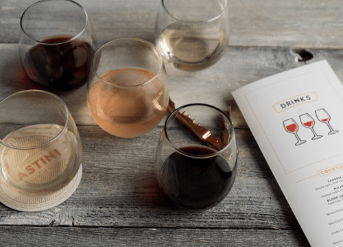 A selection of wine glasses with red, white, and rosé wines next to a drinks menu on a wooden table.