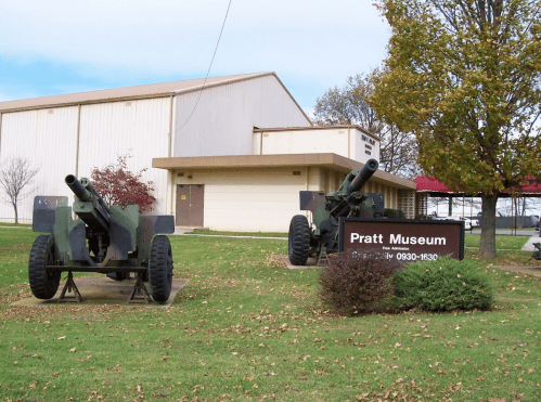 Two military cannons are displayed outside the Pratt Museum, with a building and trees in the background.