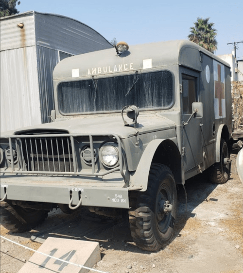 Vintage military ambulance truck parked outdoors, featuring a gray exterior and red cross markings.