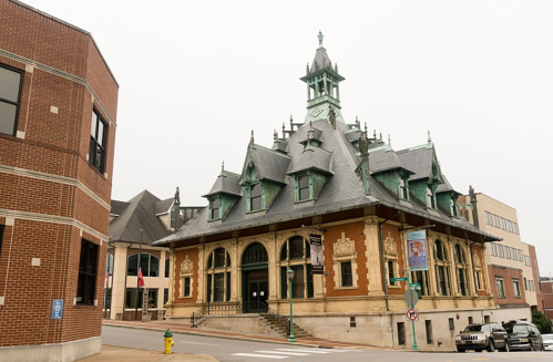 Historic building with ornate architecture, featuring a steep roof and clock tower, located at a street corner.