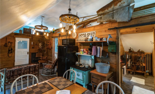 Cozy rustic interior featuring wooden walls, vintage decor, a dining table, and a mix of appliances and furnishings.