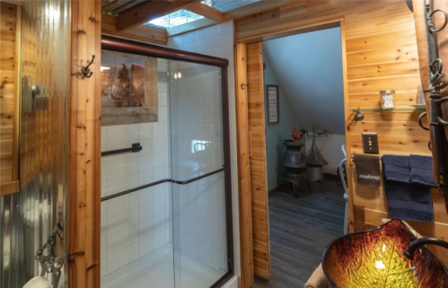 Cozy bathroom with wooden walls, a glass shower, and decorative elements, including a colorful lamp and towels.