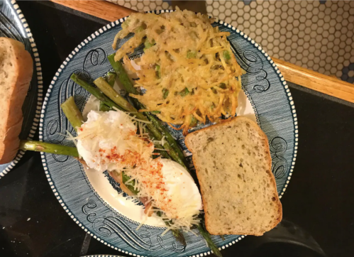 A plate with poached eggs on asparagus, a potato hash, and a slice of bread on a decorative blue plate.