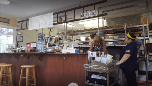 A cozy restaurant interior with a counter, menu board, and two staff members preparing food.