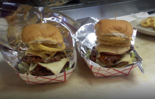 Two stacked burgers in foil-lined baskets, topped with lettuce, cheese, and onion rings.