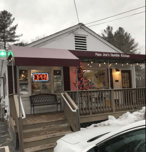 A cozy restaurant, "Papa Joe's Humble Kitchen," with an open sign and festive lights on a snowy day.