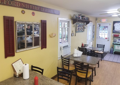 Cozy diner interior with tables, a window to the kitchen, and decor featuring local fire department memorabilia.