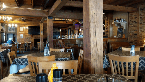 Cozy restaurant interior with wooden beams, tables set with checkered tablecloths, and a bar in the background.
