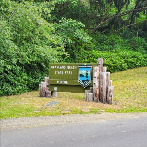 Sign for Grayland Beach State Park, surrounded by greenery, with a welcome message and park emblem.