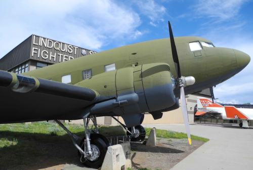A vintage military aircraft displayed outside the Lindquist Fighter Gallery, with a green exterior and prominent propeller.