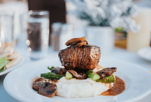 A gourmet dish featuring a tender steak atop creamy mashed potatoes, garnished with mushrooms and asparagus.