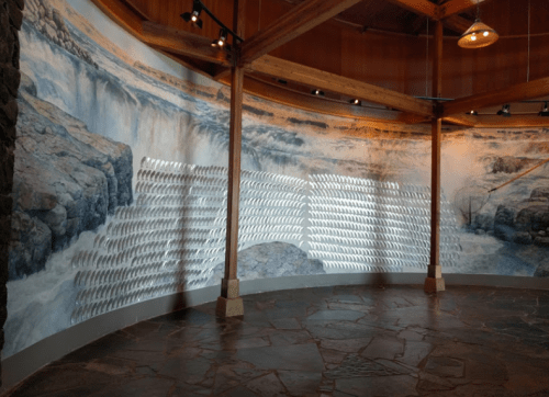 A curved wall mural depicting a waterfall, with a series of silver fish sculptures arranged in a wave pattern.