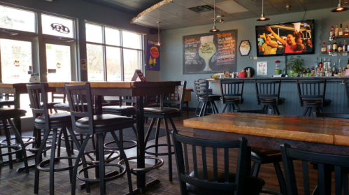 Interior of a bar with high tables and stools, a TV on the wall, and a chalkboard menu in a casual setting.