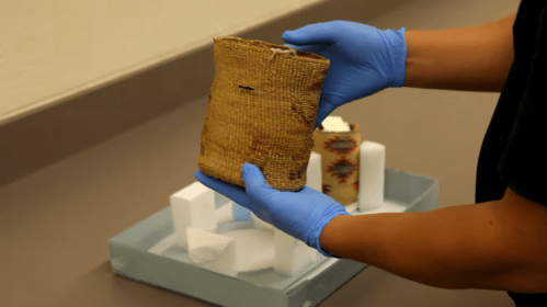 A person in blue gloves holds a woven container, with another similar item on a tray in the background.