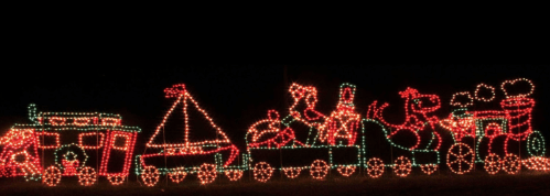Colorful holiday lights depicting a train with festive characters and a sailboat against a dark background.