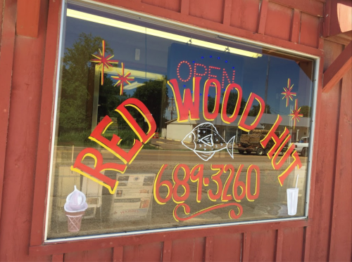 Colorful storefront window with "RED WOOD HUT" and "OPEN" signs, featuring a fish and ice cream cone illustrations.