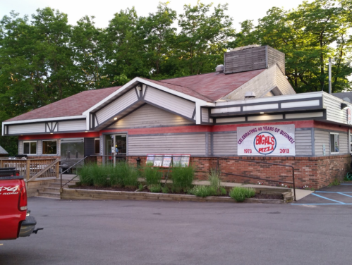 A pizza restaurant with a wooden deck, celebrating 40 years in business, surrounded by greenery.