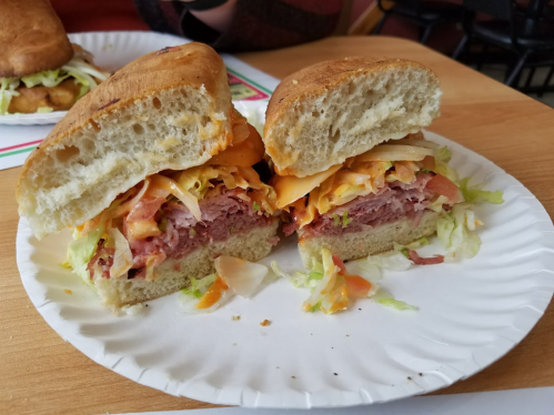 A sandwich cut in half, filled with layers of meat, cheese, lettuce, and tomato, served on a paper plate.