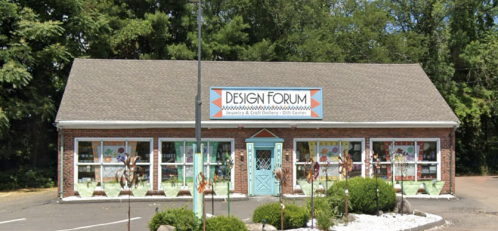 A brick building with a sign reading "Design Forum," featuring colorful windows and surrounded by greenery.