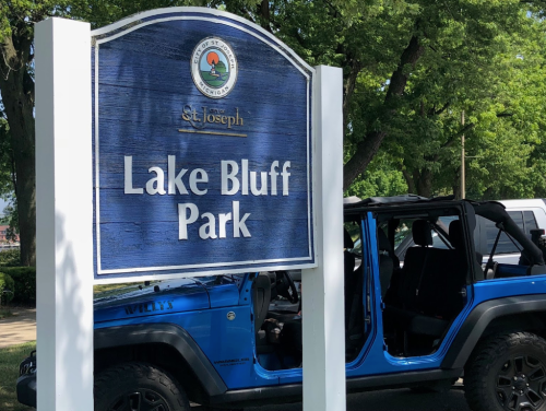 Sign for Lake Bluff Park in St. Joseph, with a blue Jeep parked nearby and trees in the background.