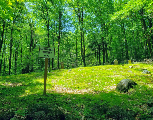 A sign for Latham-Beal Cemetery, established in 1790, surrounded by lush green trees and grass.
