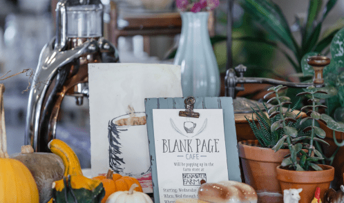 A cozy display featuring a sign for "Blank Page Cafe," pumpkins, plants, and vintage decor in a farm store setting.