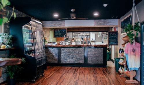 A cozy café interior with a wooden counter, plants, a drink dispenser, and a menu board, creating a welcoming atmosphere.