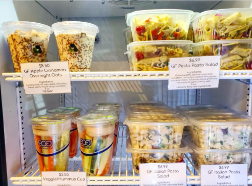 A refrigerator display with various food containers, including overnight oats, pasta salads, and a veggie/hummus cup.