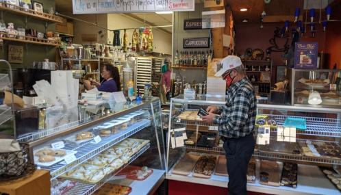 A cozy bakery with a customer browsing pastries and staff preparing food in the background.