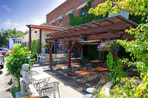 A charming outdoor dining area with wooden pergolas, tables, and vibrant flowers outside a restaurant.