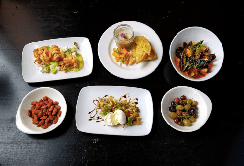A variety of dishes including shrimp, mussels, olives, and a dessert, arranged on white plates against a dark background.