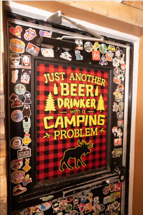 A door covered in colorful stickers featuring the phrase "Just another beer drinker with a camping problem."