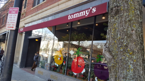 A storefront with a red awning reading "tommy's," featuring colorful decorations and a tree in front.