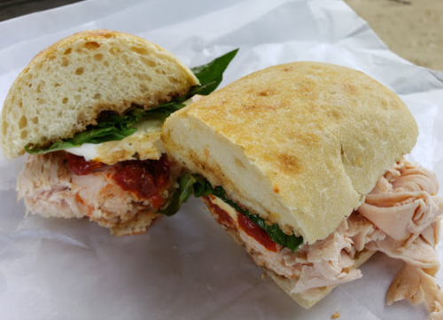 A sandwich with turkey, spinach, and sauce on a soft roll, partially cut in half, resting on white paper.
