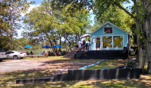 A small blue building with yellow stars, surrounded by trees and outdoor seating, on a sunny day.