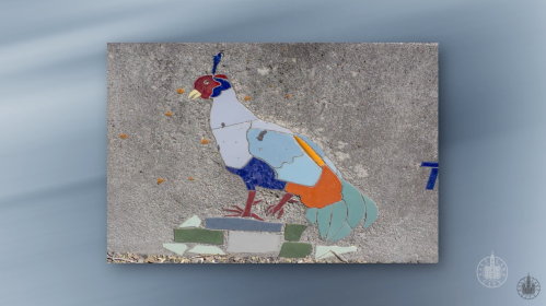 A colorful mosaic of a peacock standing on a stone base, featuring vibrant blue, orange, and green tiles.