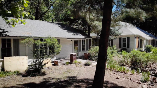 A serene view of a house surrounded by trees and greenery, with a clear blue sky above.