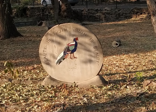 A stone plaque in a park featuring a colorful bird and the inscription "Beauty is truth, truth is beauty."