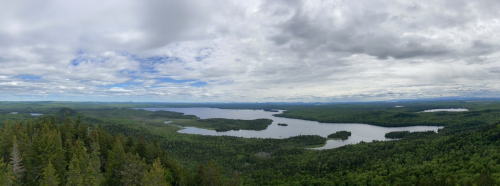 A panoramic view of a lush green landscape with lakes under a cloudy sky.
