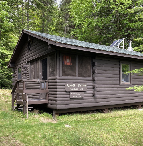 A rustic ranger station made of dark wood, surrounded by lush green trees at Alleghasp Lake.