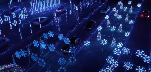 Aerial view of a festive light display with blue snowflakes, trees, and cars driving through a winter wonderland.