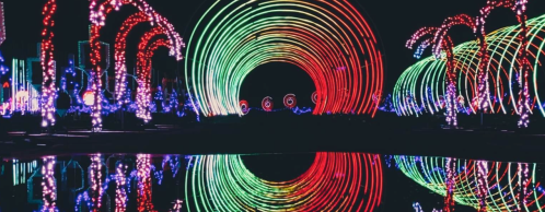 Colorful circular light patterns reflect on water, creating a vibrant, festive atmosphere at night.