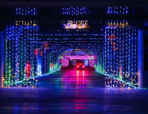 A colorful tunnel of holiday lights with vibrant blue, green, and red decorations illuminating the pathway.