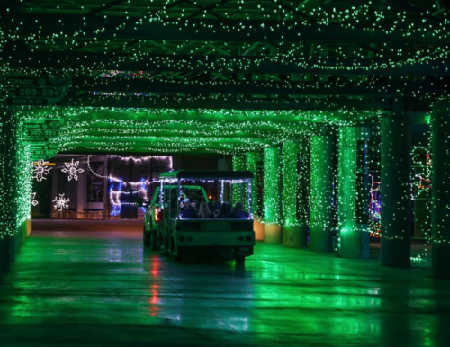 A festive tunnel illuminated with green lights, with a small vehicle driving through.